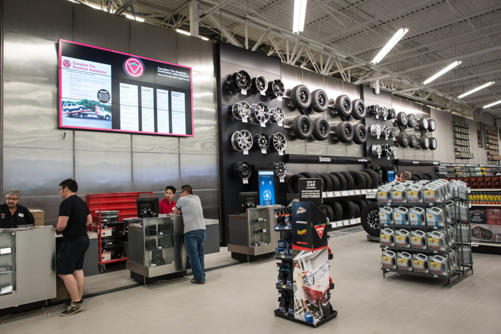 Seção automotiva de uma loja da Canadian Tire mostrando um balcão com funcionários e clientes, com pneus na parede atrás.