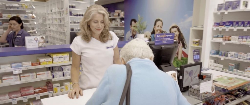 A pharmacist stands at a counter facing a customer.