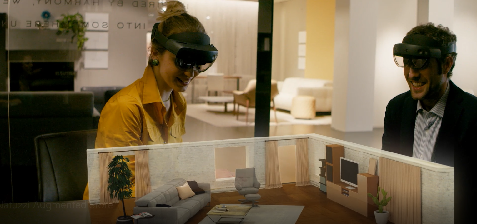 A woman and man wearing HoloLens2 headsets look at a scale model of a living room.