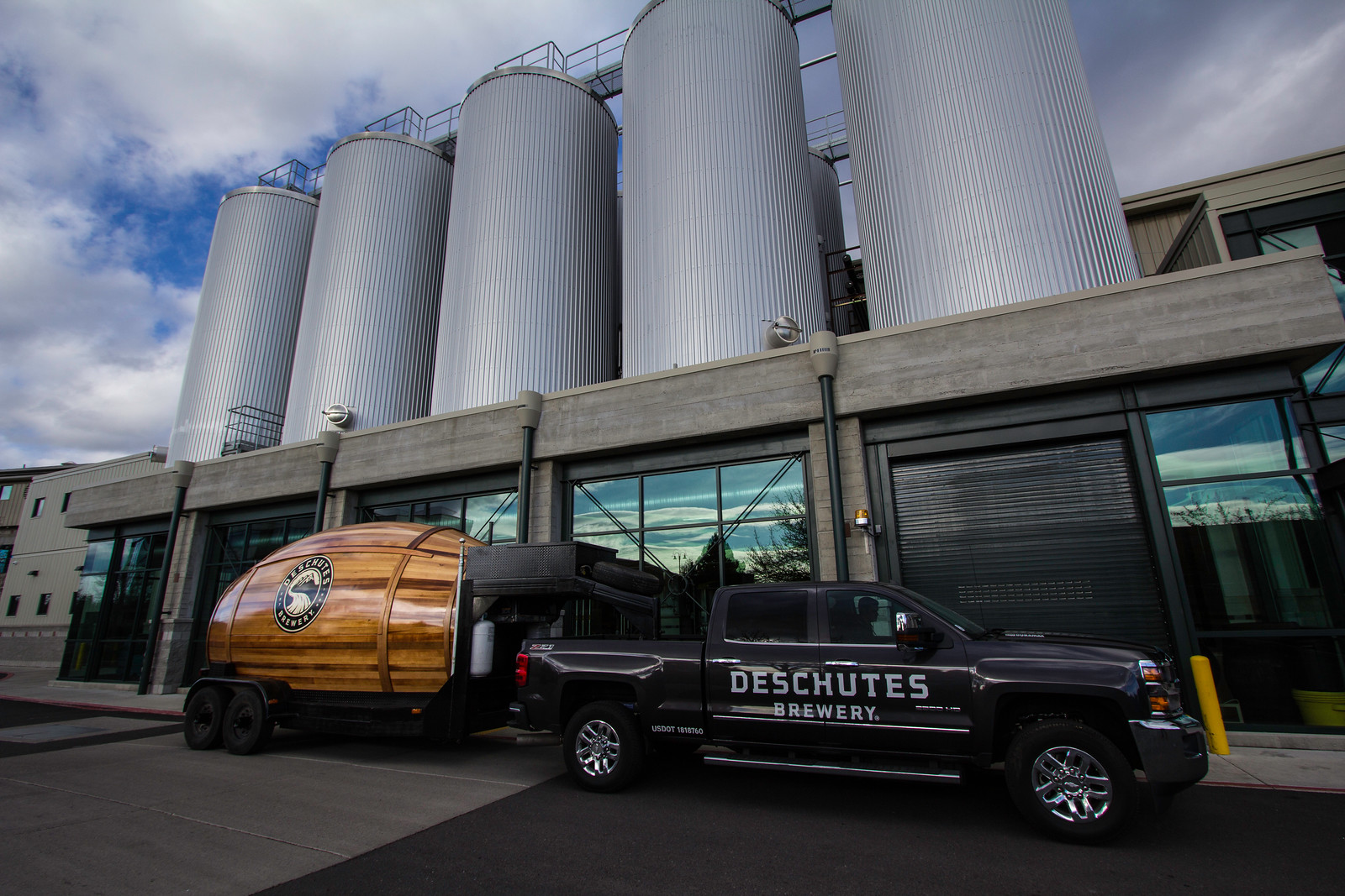 A pickup truck towing a giant beer keg is parked in front of a Deschutes brewery.