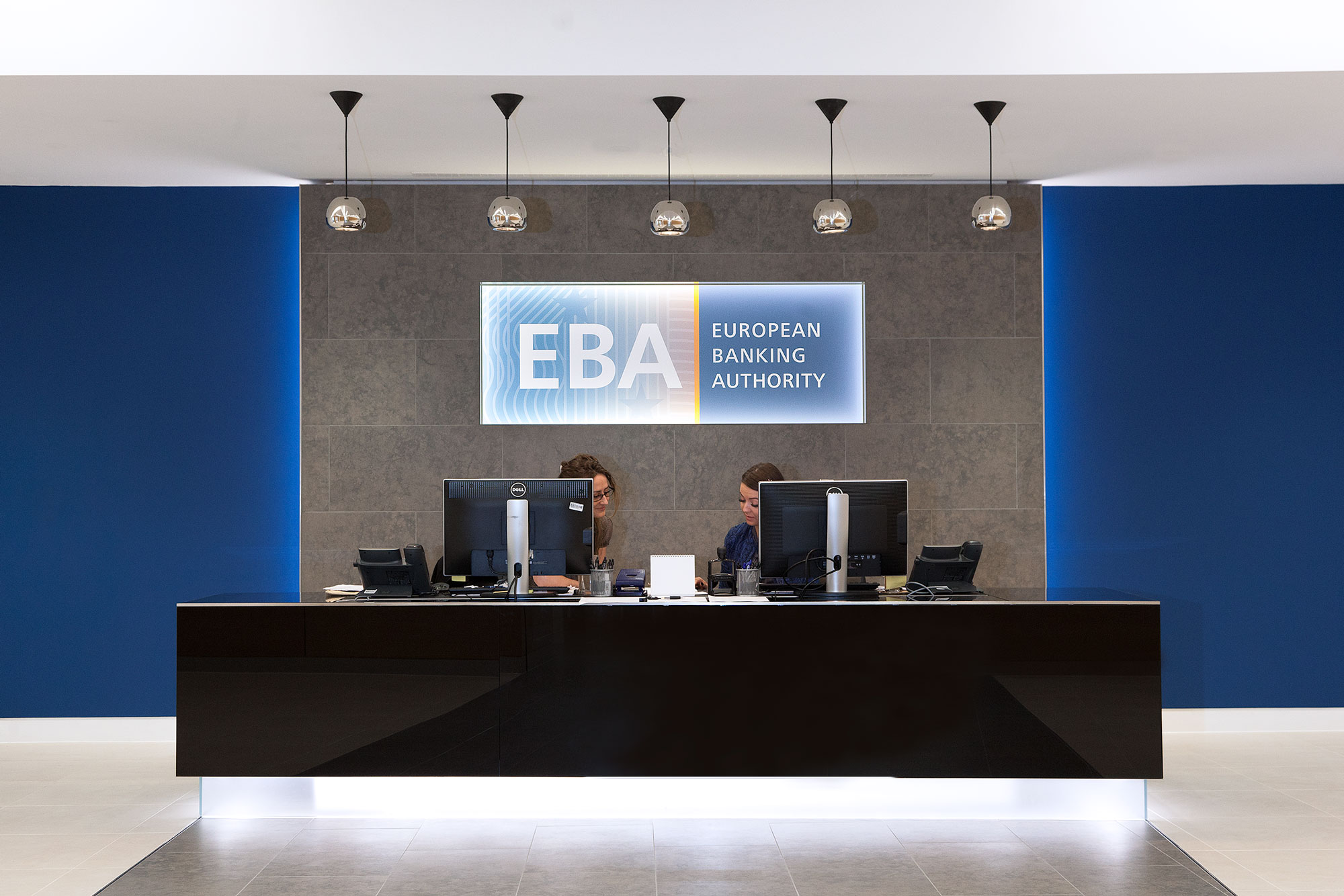 Photo showing a reception desk with two employees and computers at the European Banking Authority.