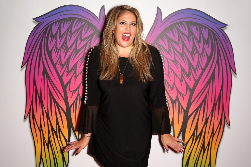 A woman stands in front of a wall that has a colorful angel wing design