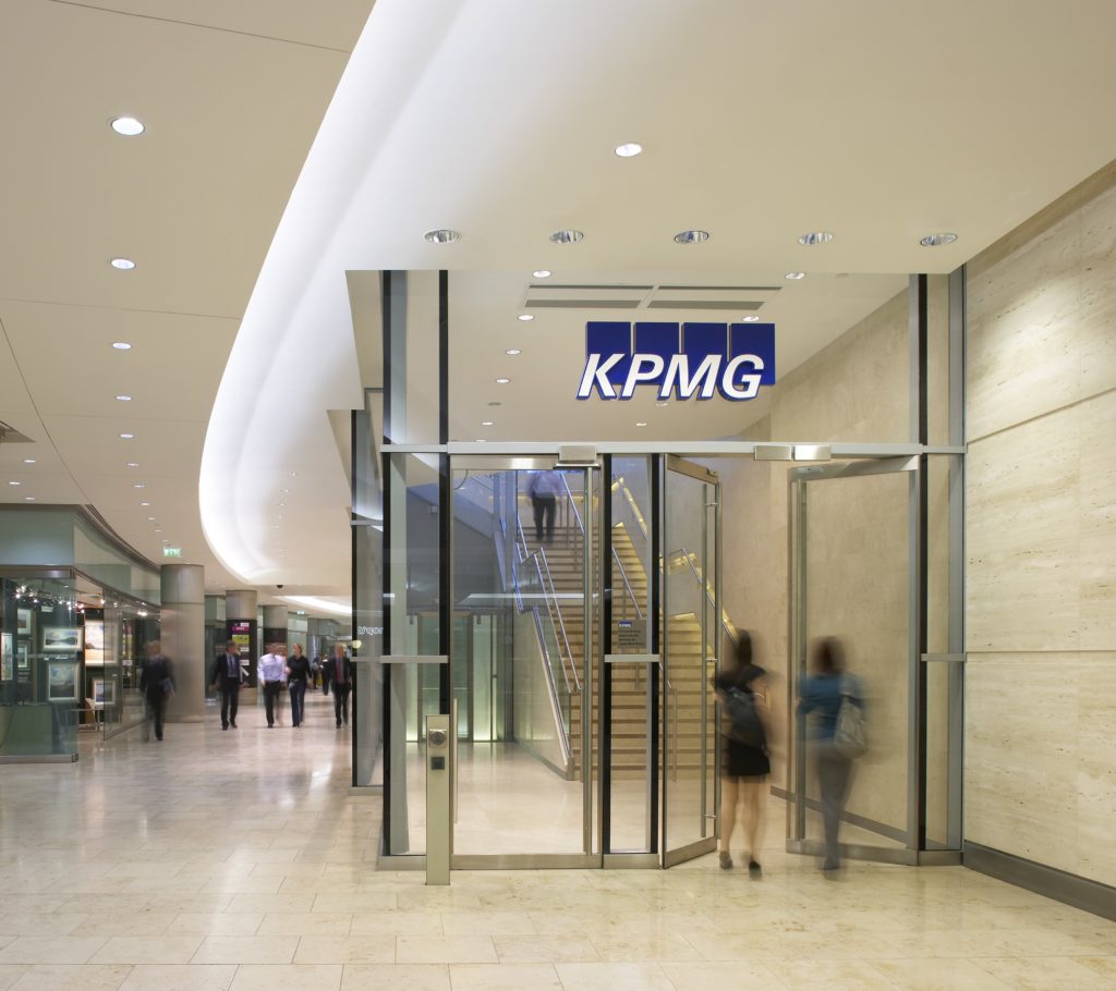 Office workers walk into a KPMG office through a glass door inside a building.