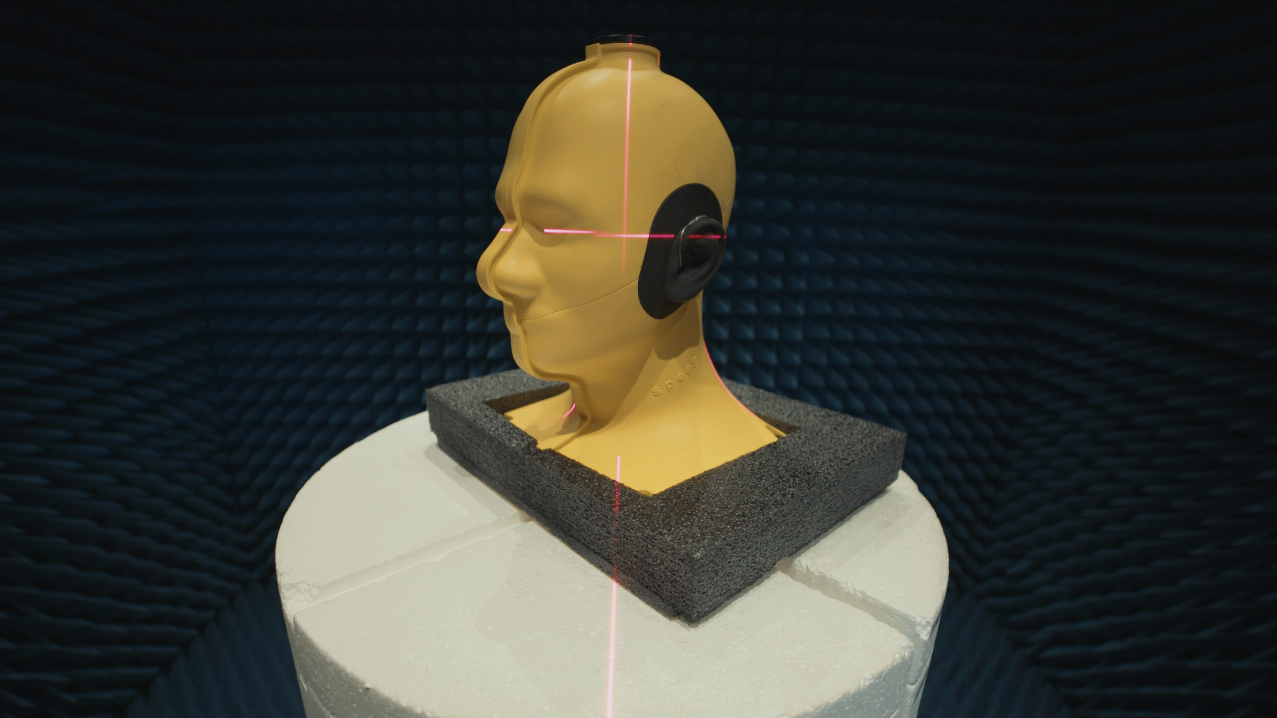 Photo of yellow mannequin head on a white stand, displaying a hearing aid device.