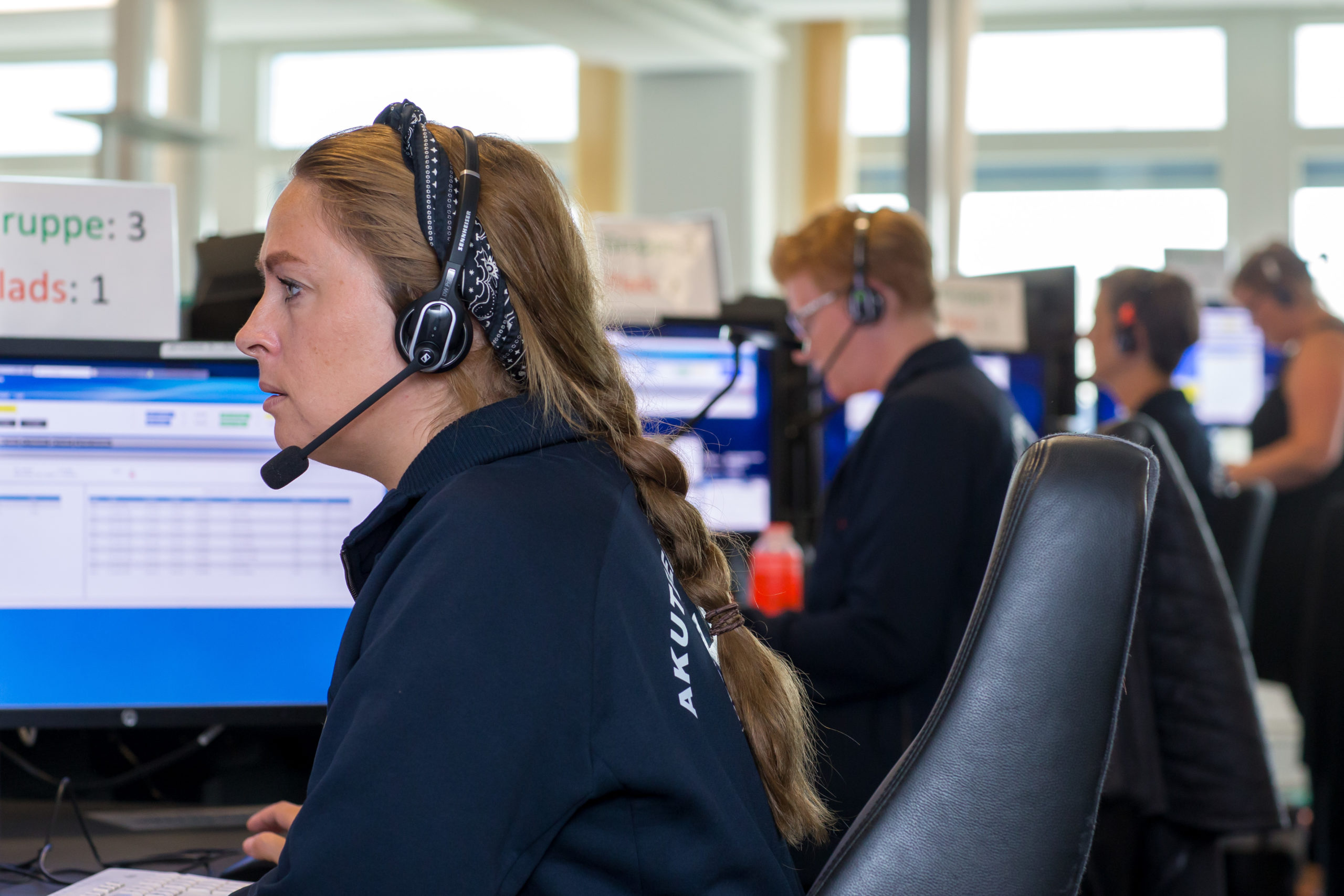 Photo showing row of four employees at Emergency Medical Services Copenhagen, wearing headsets and sitting in front of computers.