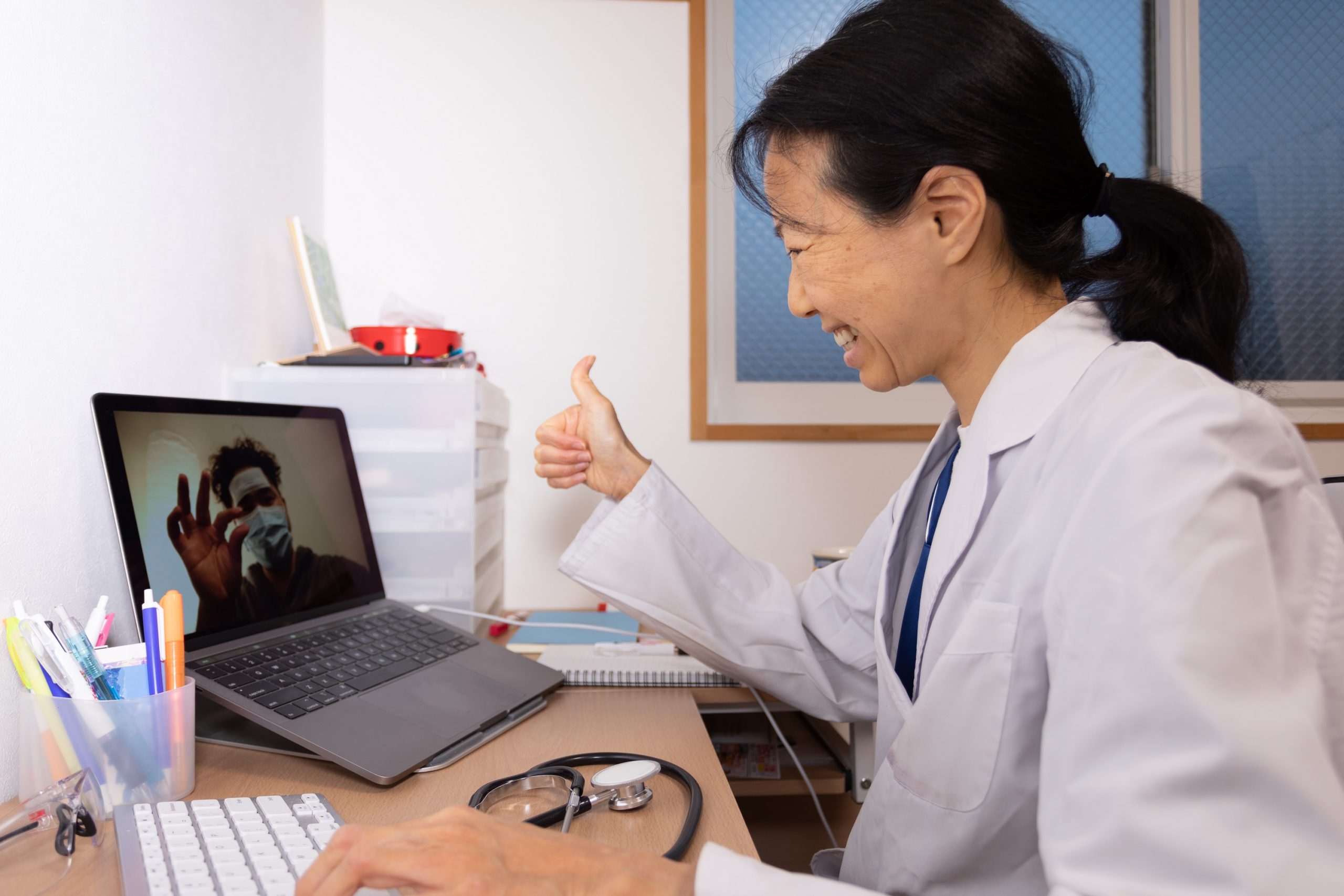 Photo of a smiling woman wearing a white medical coat and sitting in front of a computer, giving a thumbs-up.