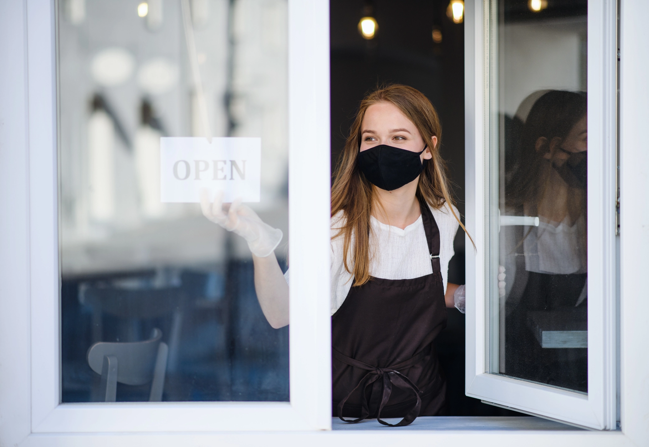 A woman wearing a mask turns the Open sign in a window