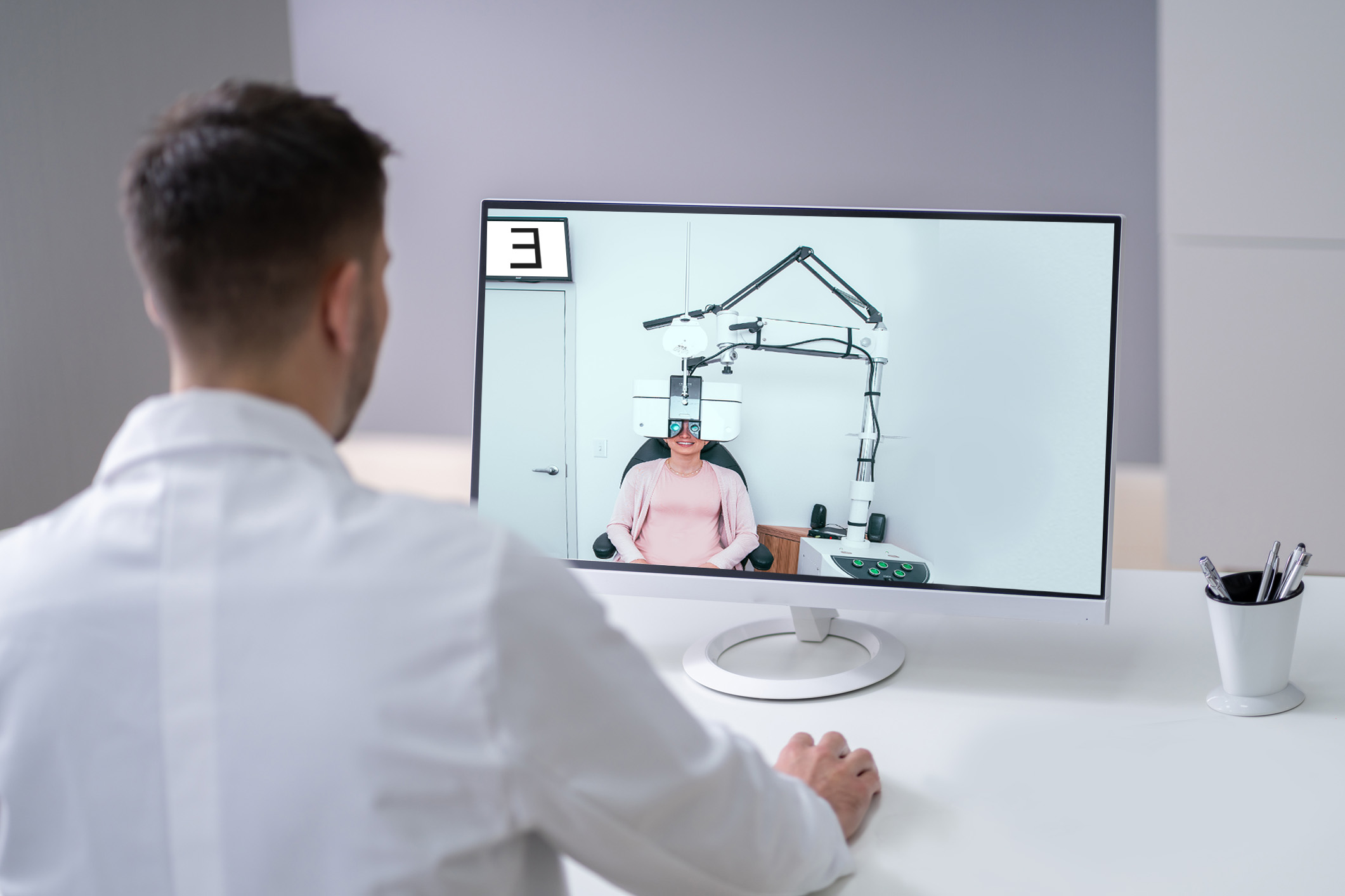 An eye doctor looks at a screen that shows a patient wearing a device that tests their vision.