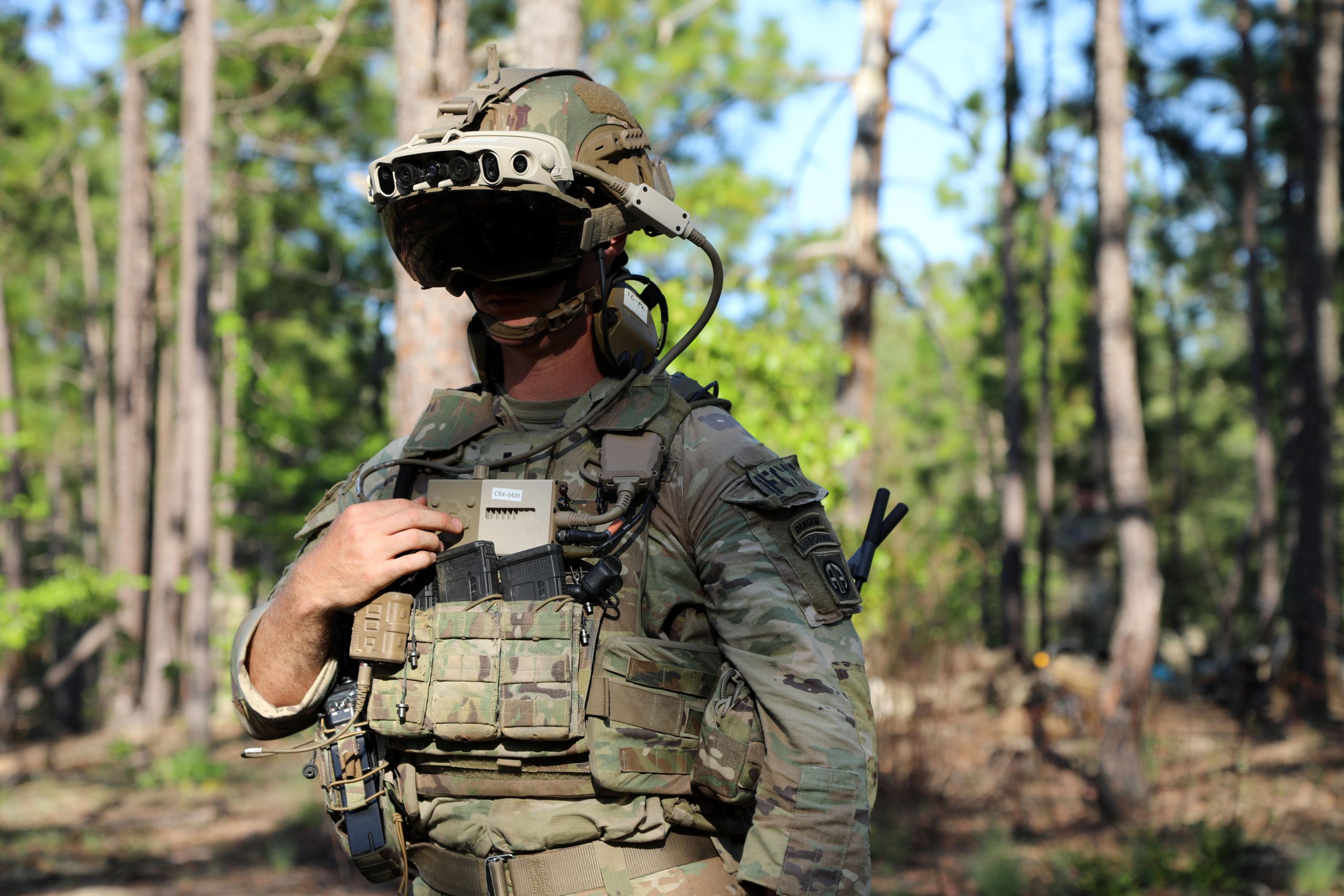 Photo of a male U.S. Army soldier standing in a wooded area and wearing a HoloLens headset.