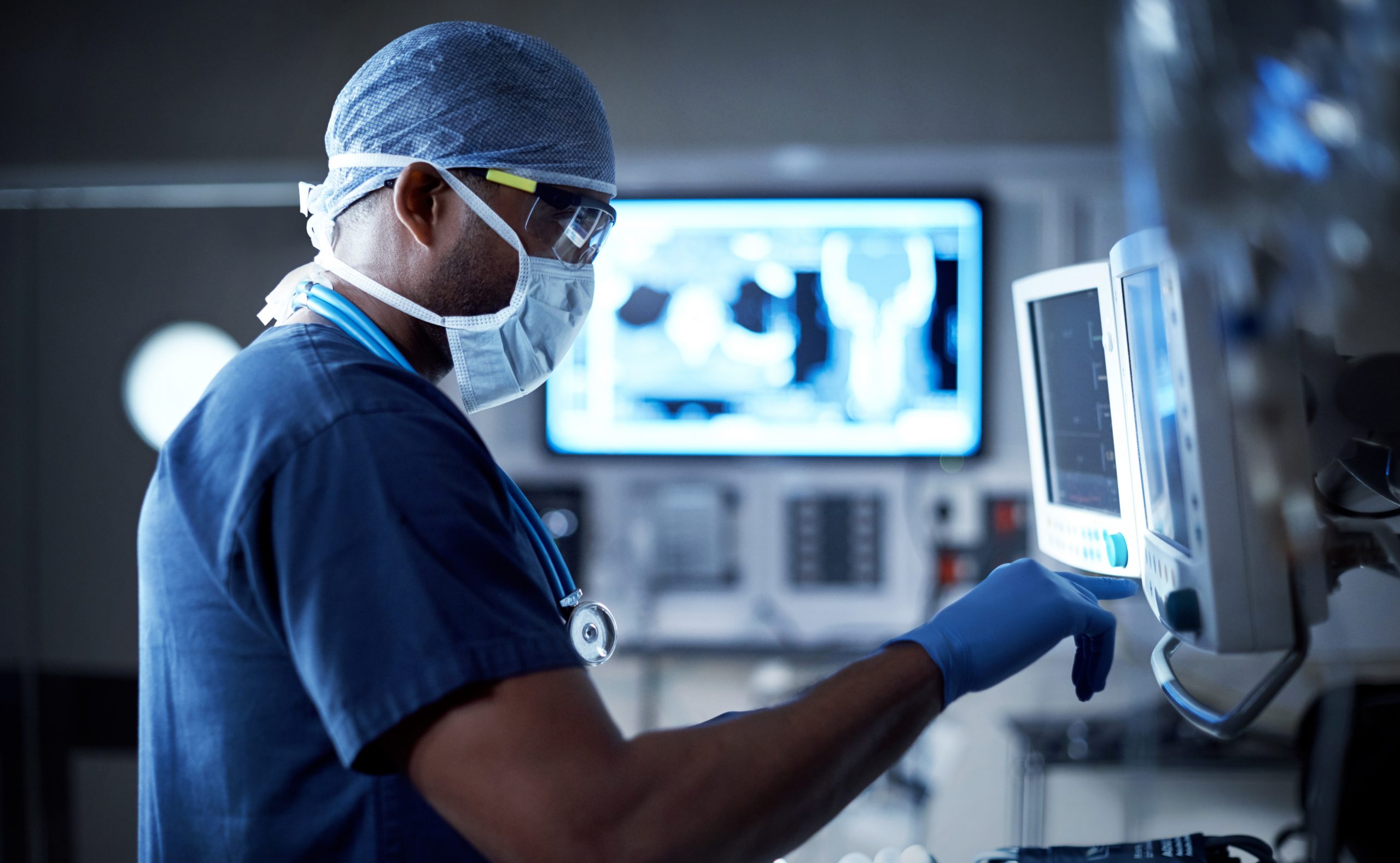 Photo of a doctor standing in a darkened surgical suite, touching a computer screen.