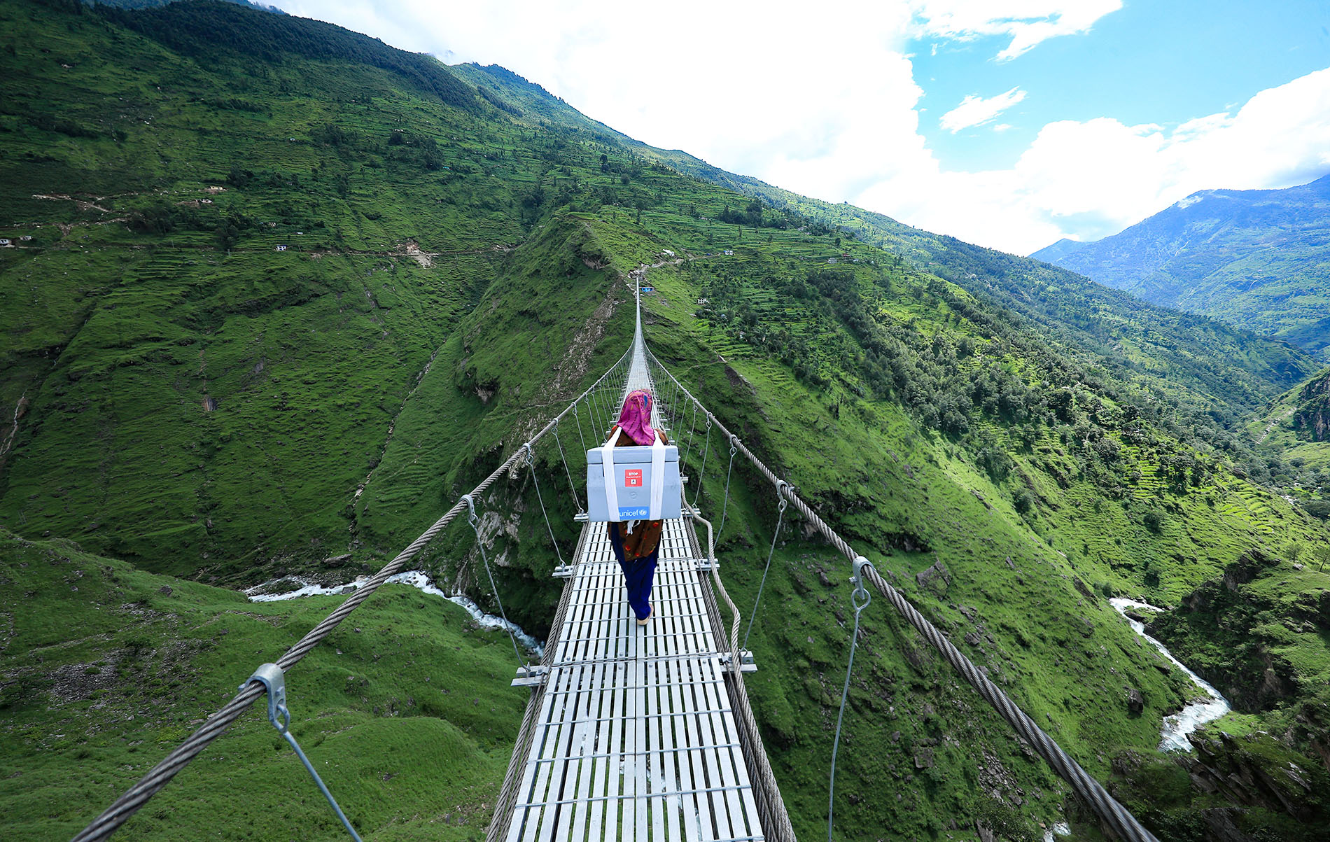 A health care worker in Nepal walks across a bridge