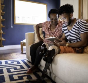 Smiling mother watches son who is an amputee gets involved with what's on his tablet device