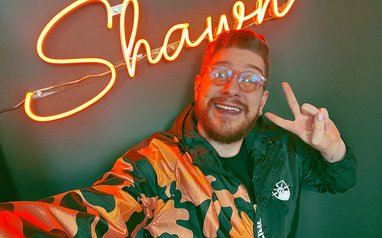 Man stands in front of a "Shawn" sign smiling