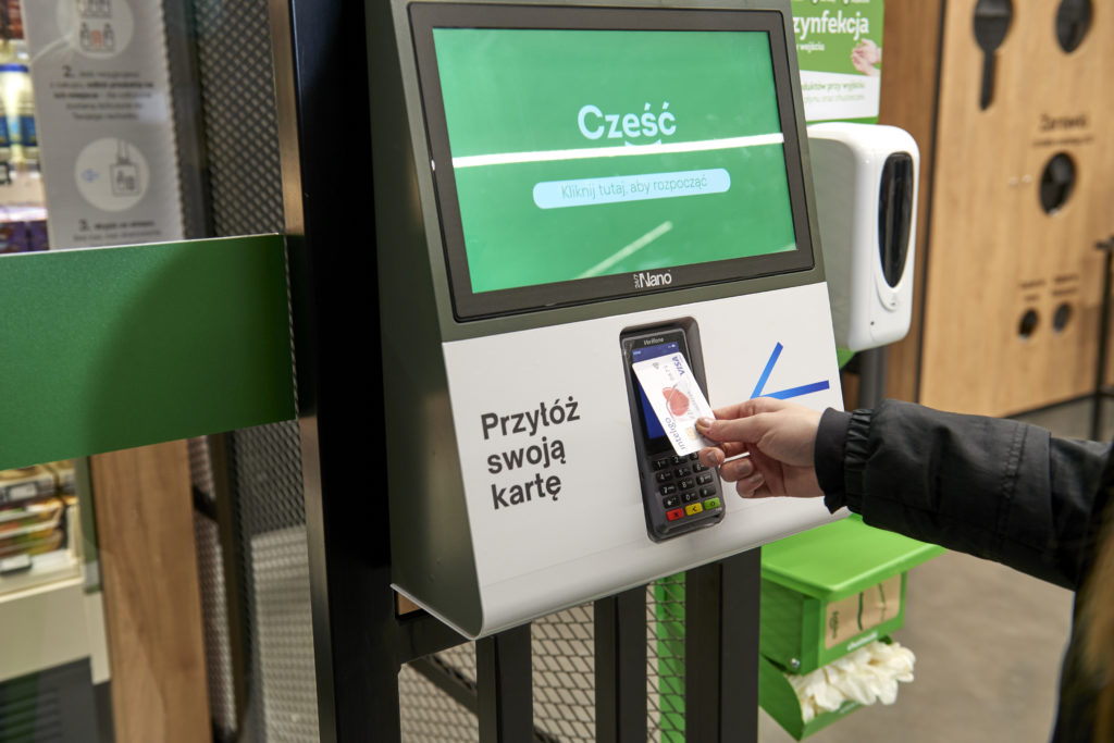 A shopper's hand inserts a bank card into a Zabka entry portal. 