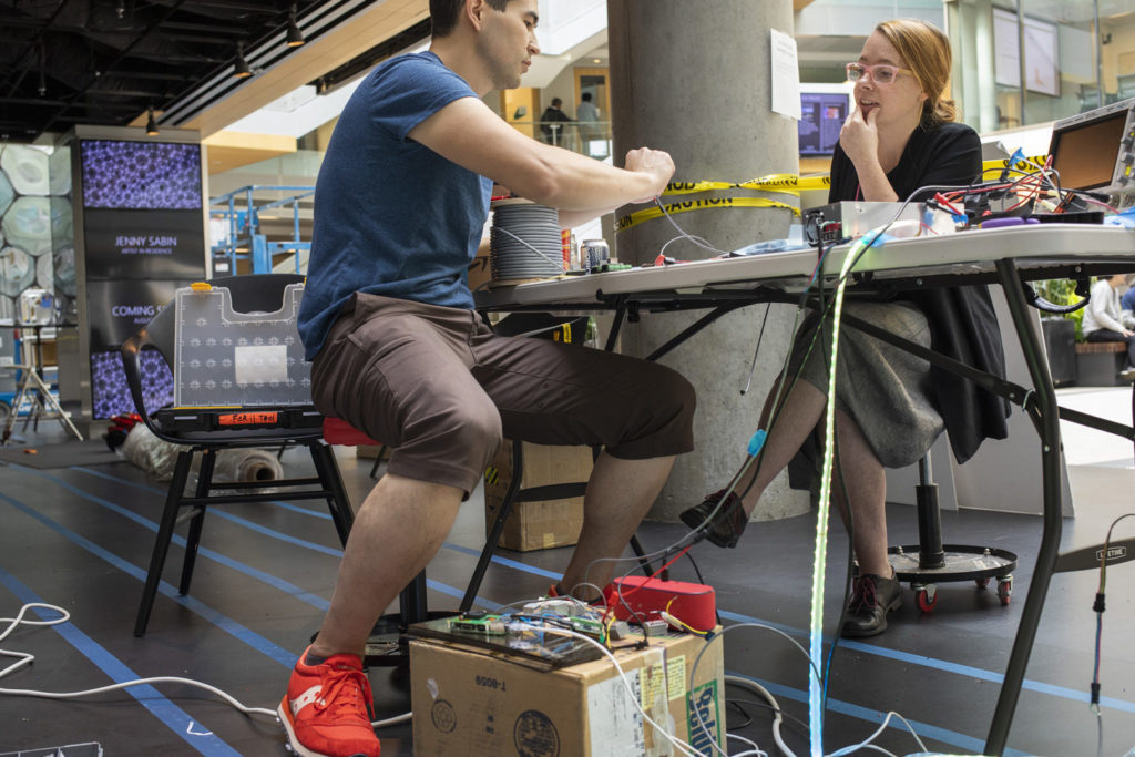 Jonathan Lester, left, principal electrical engineer at Microsoft’s research lab in Redmond, Washington, and Asta Roseway, right, a principal research designer who runs the Artist in Residence Program, prepare LED lights to embed in Ada’s fabric. Photo by John Brecher for Microsoft. Electrical engineer Jonathan Lester and Asta Roseway sit at a table preparing LED lights