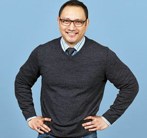 Jean Lozano stands in front of a blue background with his arms on his hips
