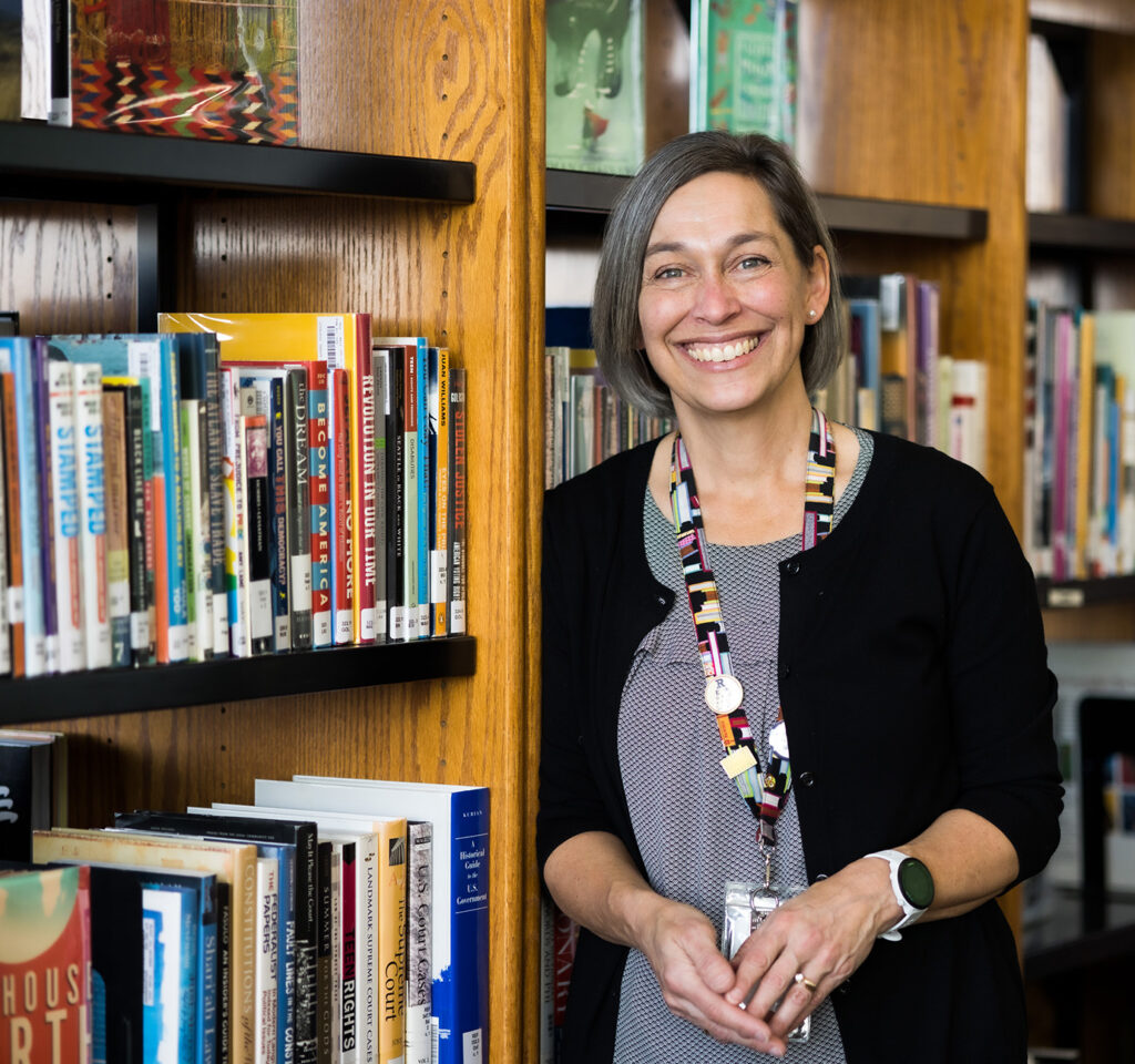 Woman smiles and leans on a bookshelf