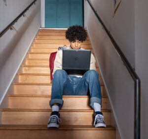 Young mn sitting on a staircase working at his laptop computer