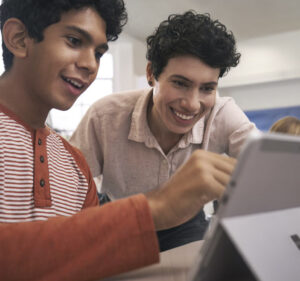 Two high school age boys interacting with what's on their laptop computer