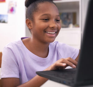 A teenage girl smiles as she reads what's on her laptop computer