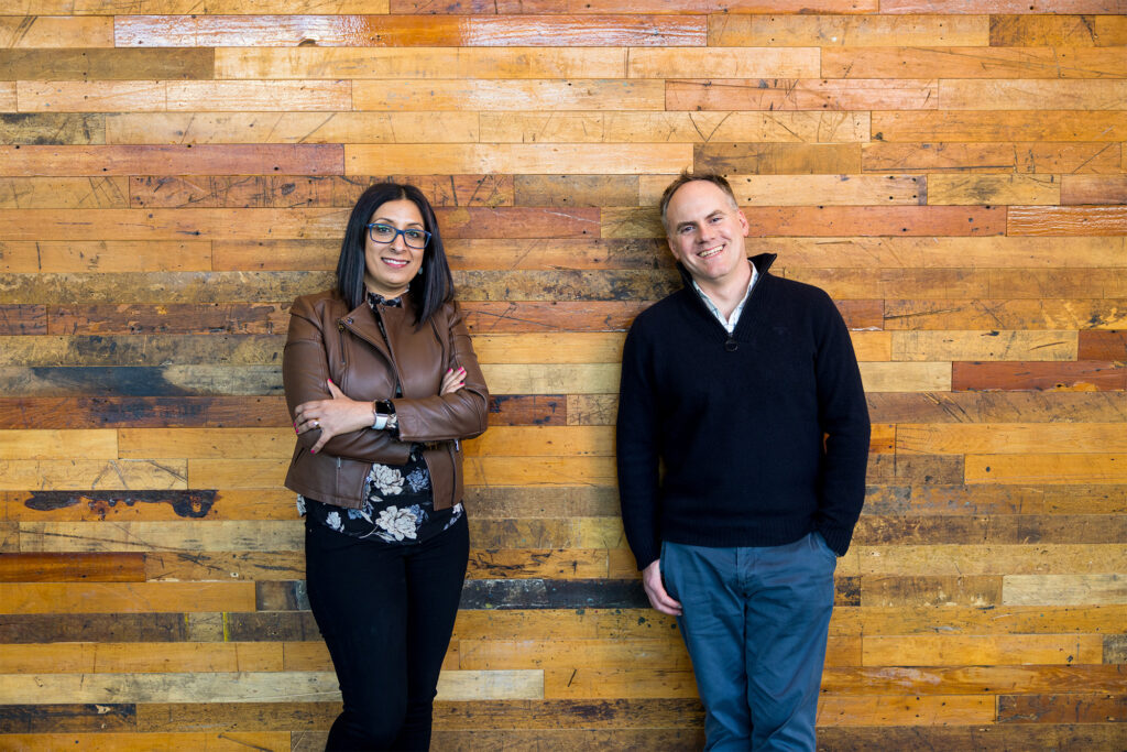 Nidhi Chappell, Microsoft head of product for Azure high performance computing, and Phil Waymouth, Microsoft principal program manager in charge of strategic partnerships. Nidhi is on the left, Phil on the right. They are standing against a wood wall.