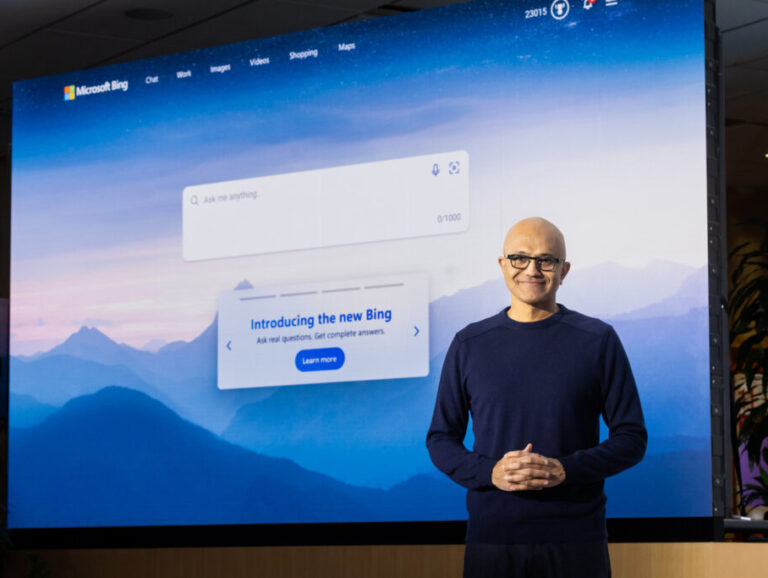 Man smiles as he stands in front of a large screen introducing the new Bing