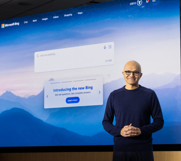 Man smiles as he stands in front of a large screen introducing the new Bing