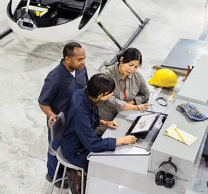 Three workers in a helicopter factory look at what's on the screen of a tablet computer