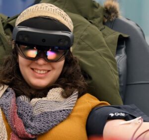 A blood donor squeezes a ball with her left hand while wearing a mixed reality device during her donation at a blood center.