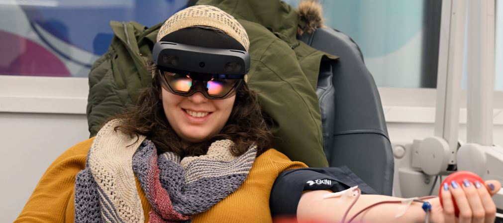 A blood donor squeezes a ball with her left hand while wearing a mixed reality device during her donation at a blood center.