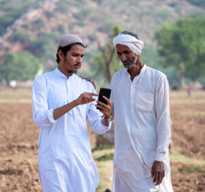 Two farmers standing in an arid village field looking at a mobile phone.