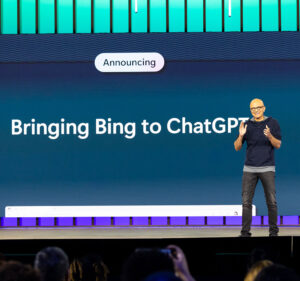 Microsoft Chairman and CEO Satya Nadella clapping onstage at Build 2023 with text behind him reading Announcing Bringing Bing to ChatGPT