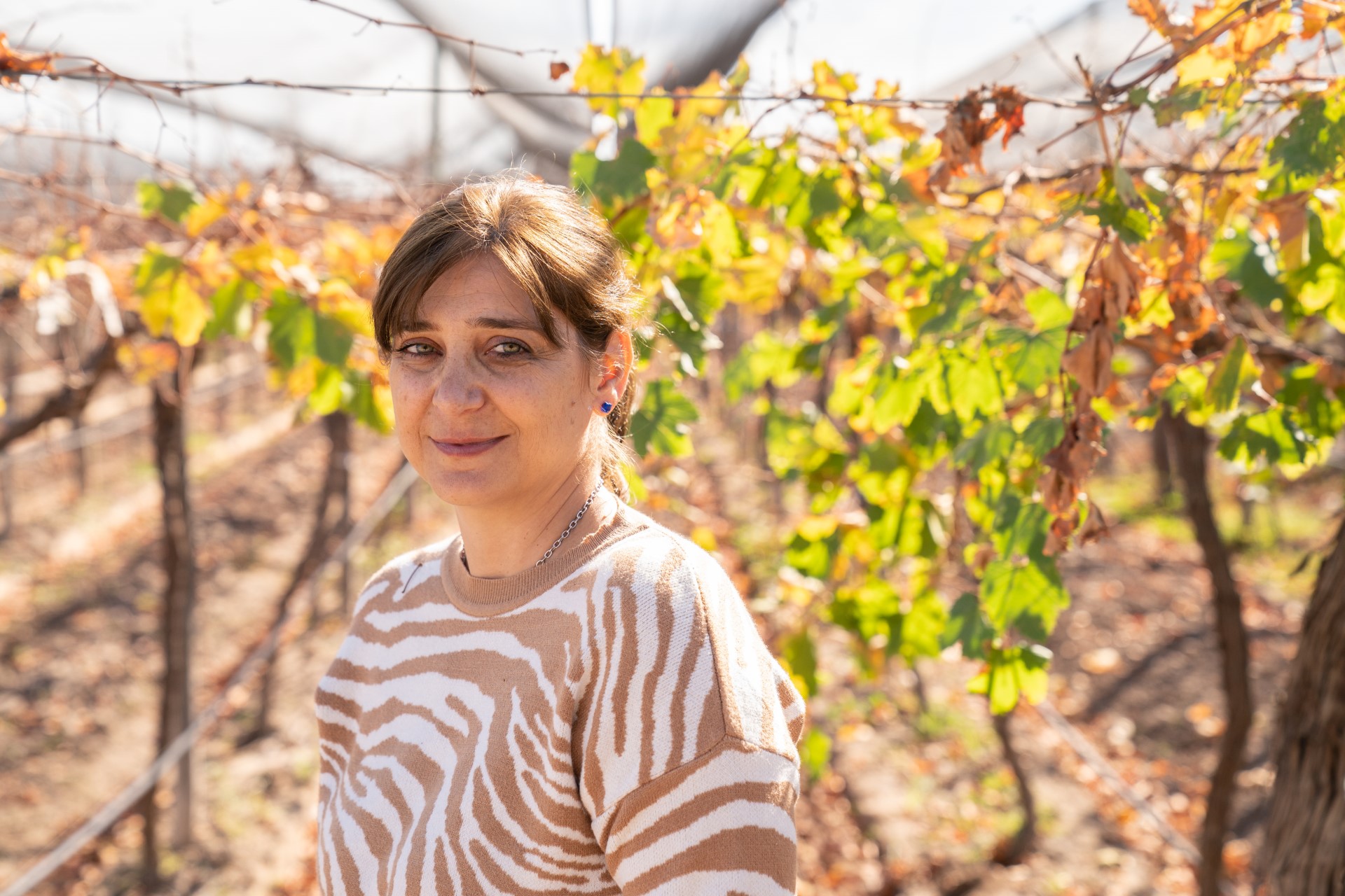 A woman smiles while standing in a vineyard