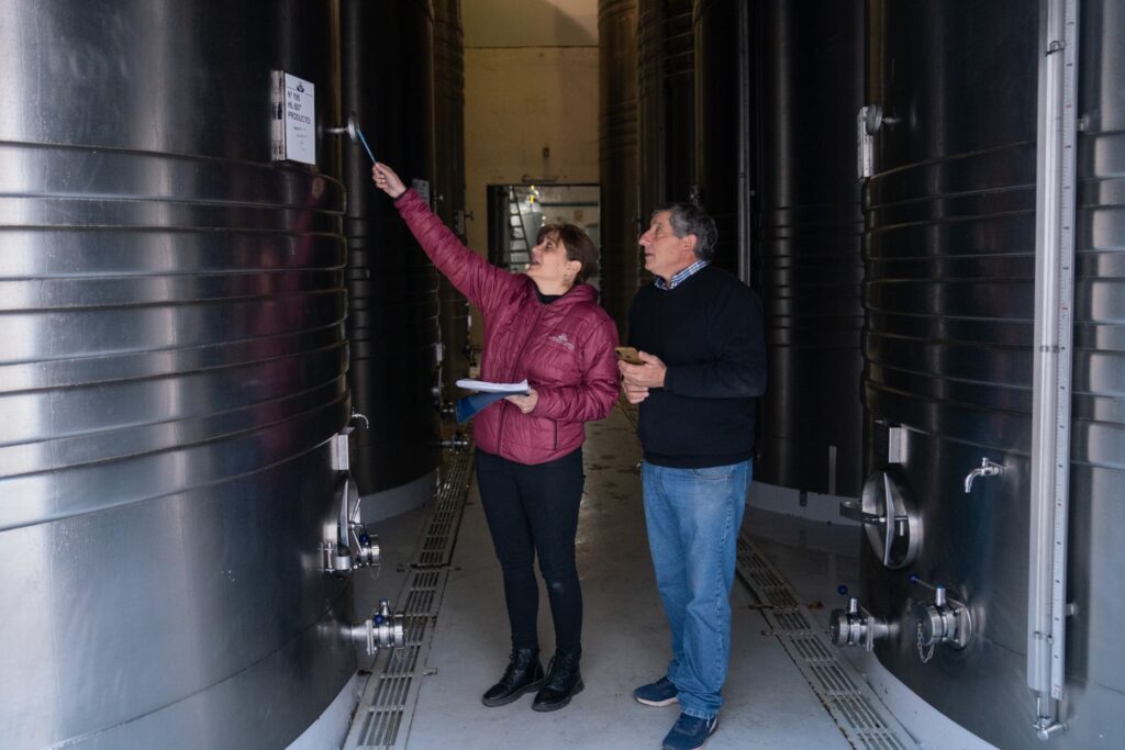 A woman and a man look up at a large steel vat of wine