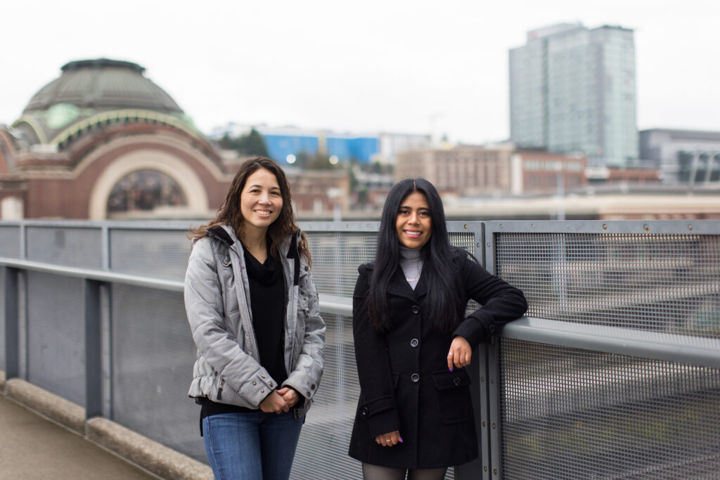 Two women stand on a bridge smiling