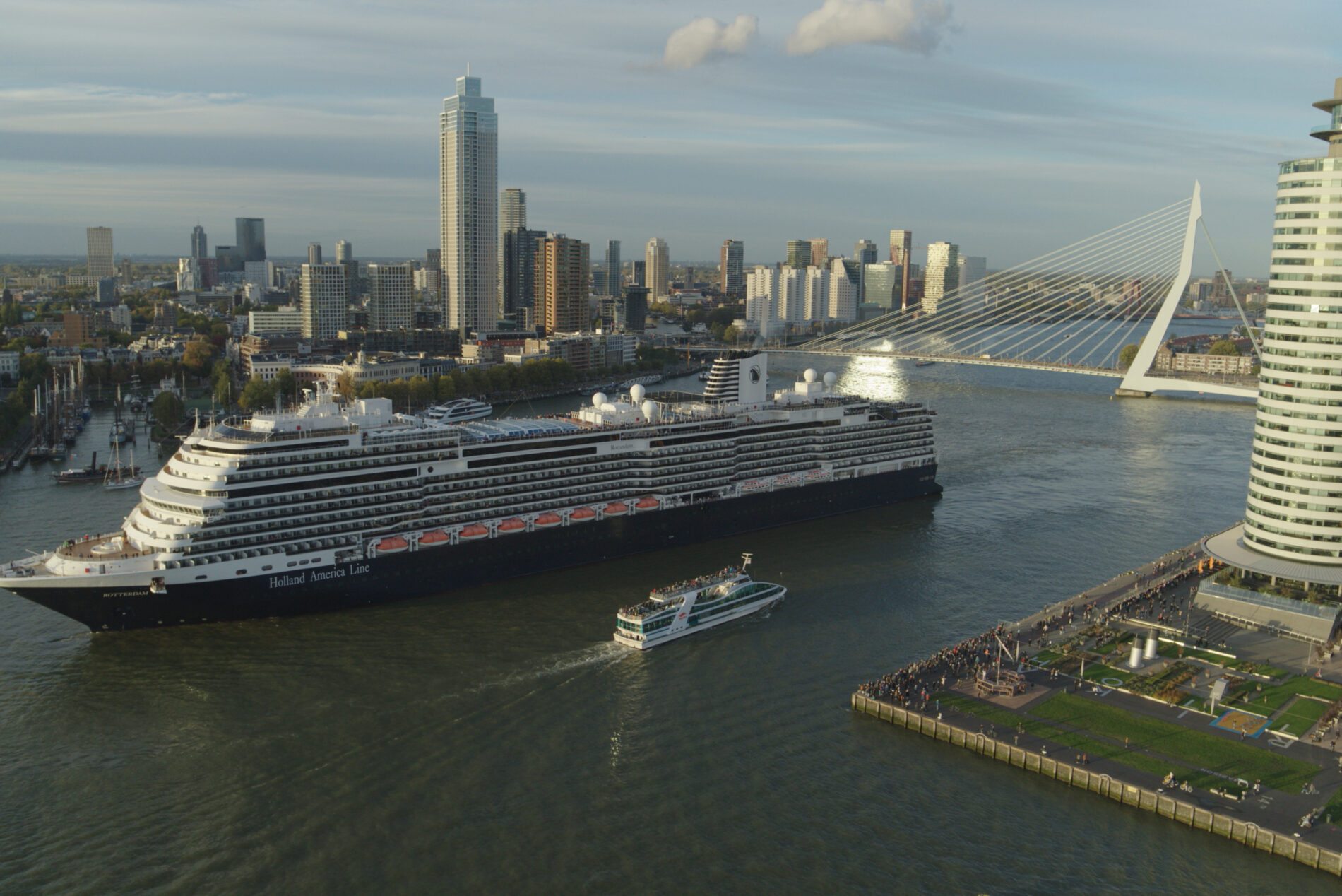 The cruise ship Rotterdam departs an urban port during daylight hours.