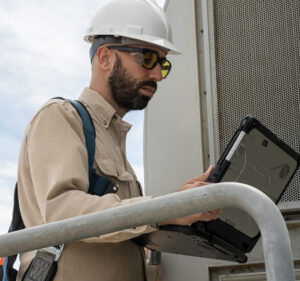 Man earing a hardhat and holding a tablet device as he works outdoors