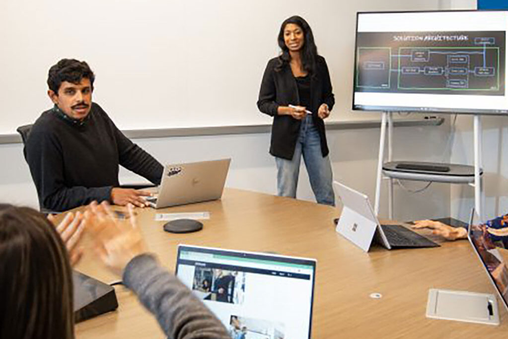 Woman presenting in front of other employees seated around a table in a conference room at the new AI Co-Innovation Lab in San Francisco