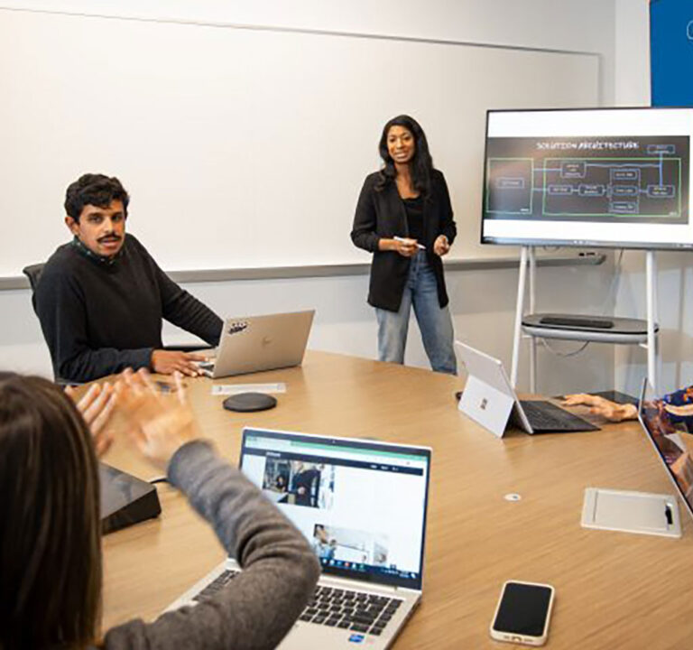 Woman presenting in front of other employees seated around a table in a conference room at the new AI Co-Innovation Lab in San Francisco