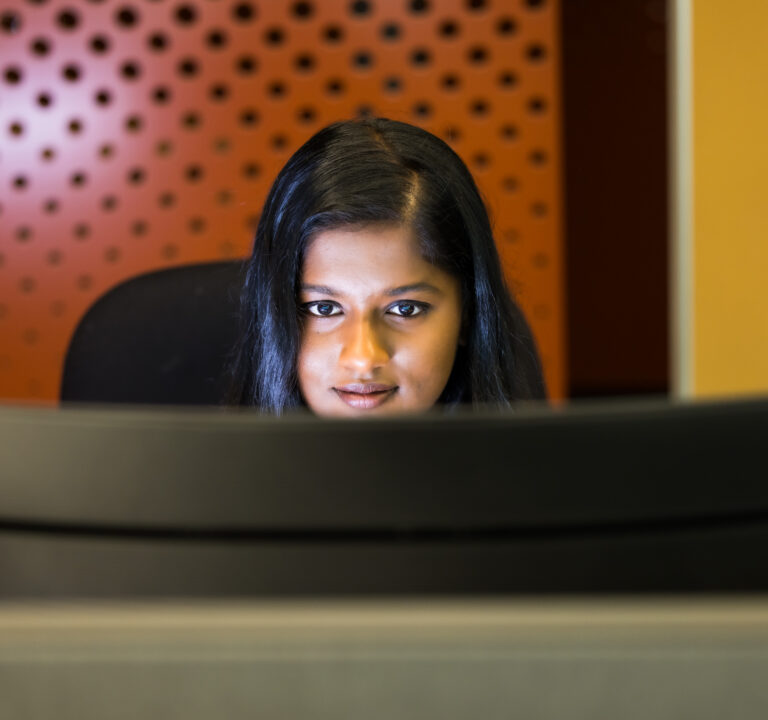 A woman sits at a desk looking at a computer monitor