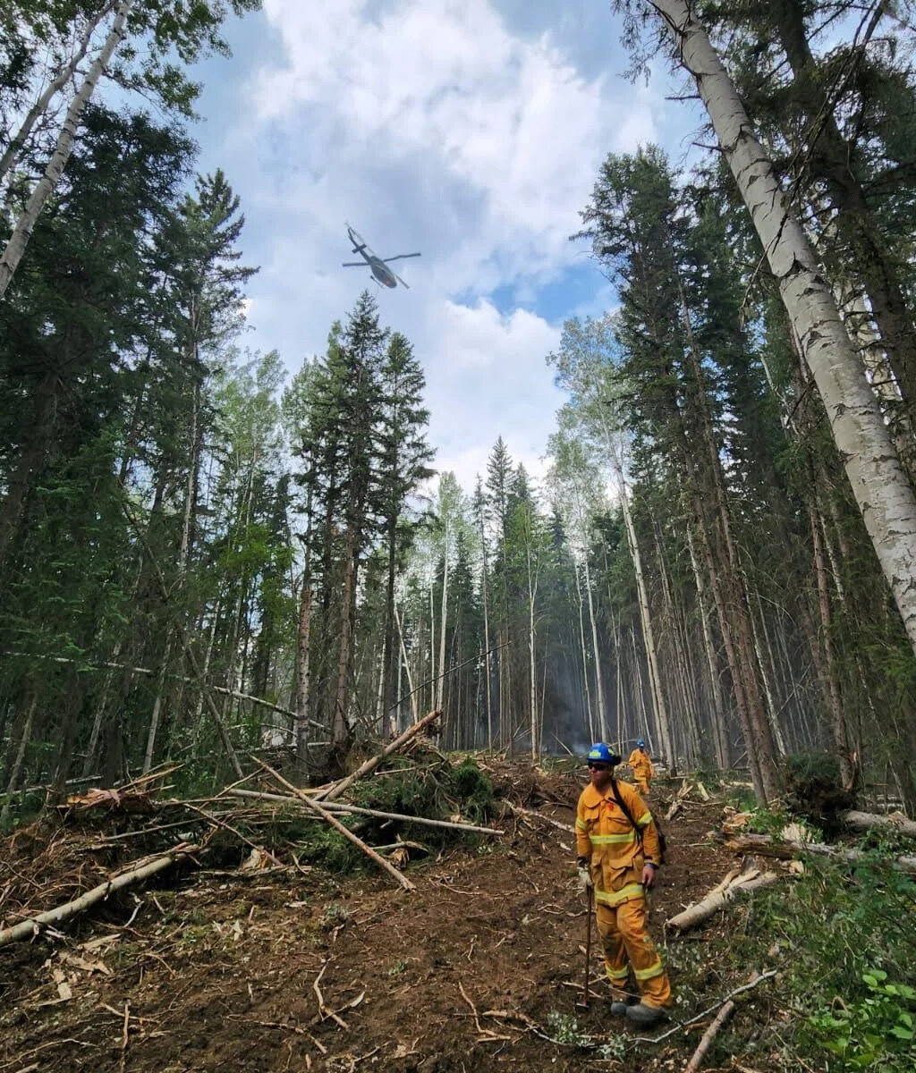 Two firefighters in a forest clearing with a helicopter overhead