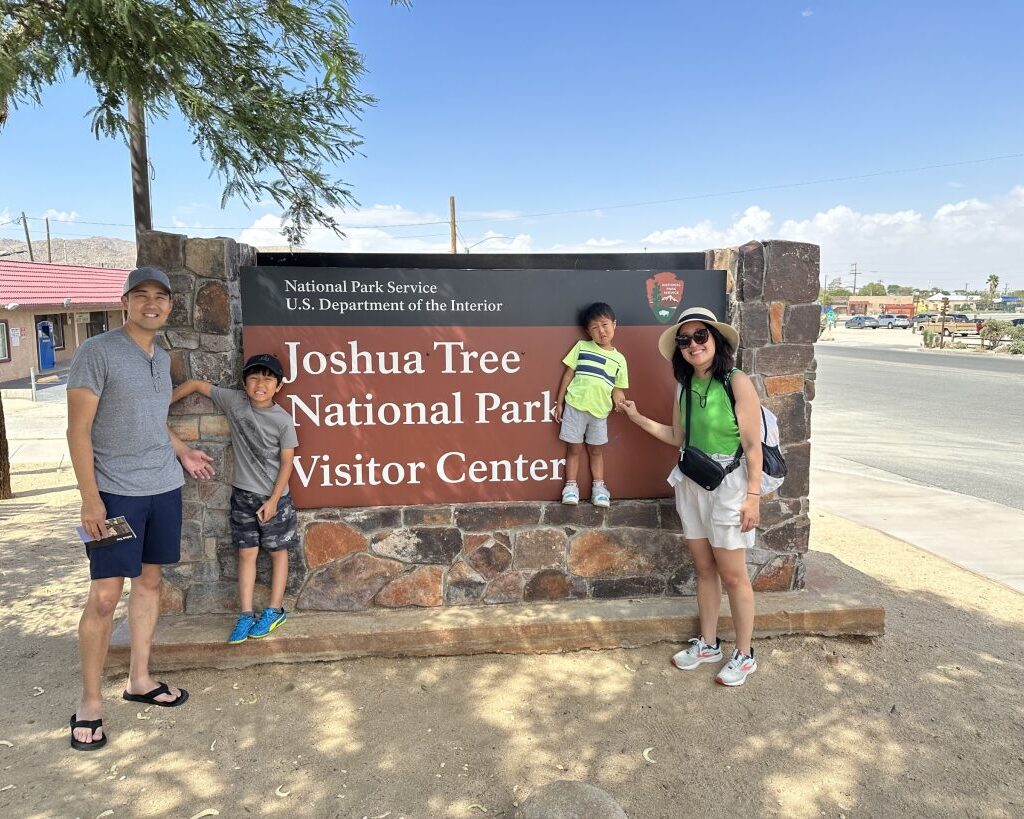 A family stands in front of a Joshua Tree National Park Visitor Center sign
