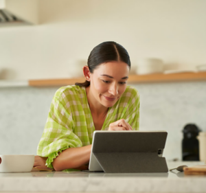 Woman in her kitchen smiling as she enters something into her tablet device