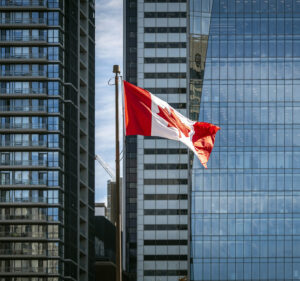 Canadian flag with skyscraper buildings behind it