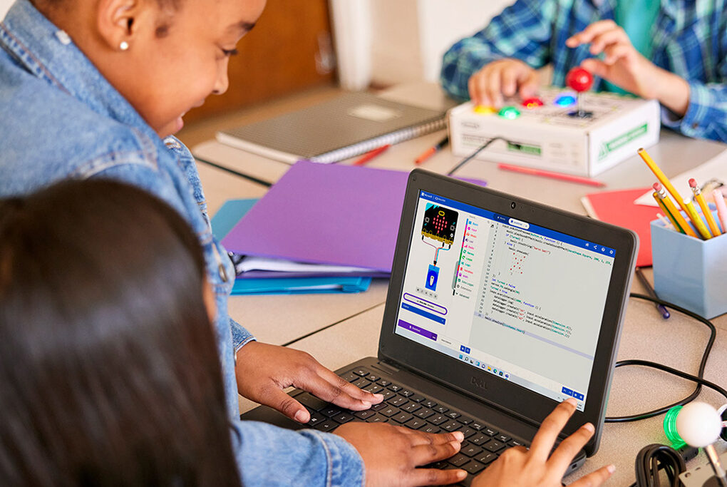Two girls share a laptop computer in a classroom