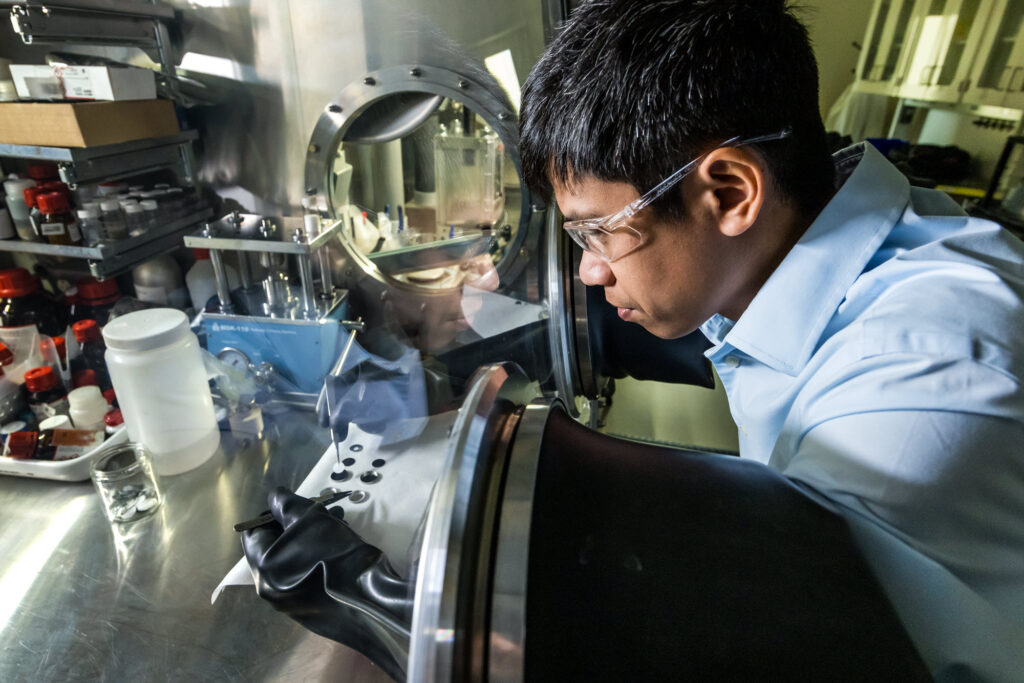 一位男性科学家用手组装硬币电池，用镊子将其放入合成的固体电解质中。