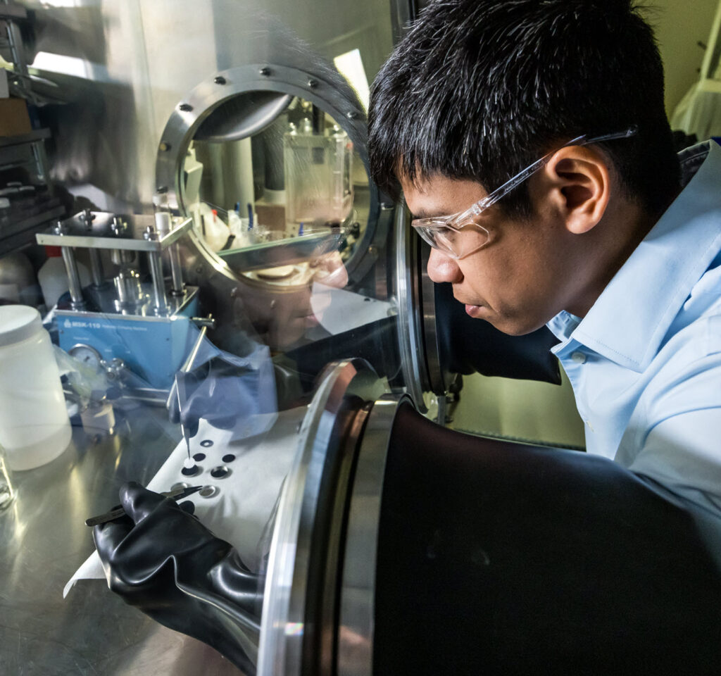 A male scientist assembles a coin cell by hand, using tweezers to drop in the synthesized solid electrolyte.