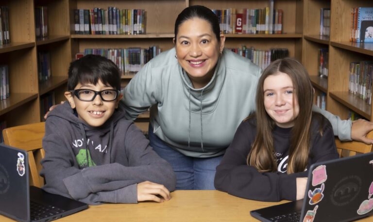 Joshua Munoz, Ana Ruiz and Martina Della Siega sit at a table in a school library looking ahead and smiling.