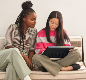 Two young women sitting on a couch and sharing a laptop computer