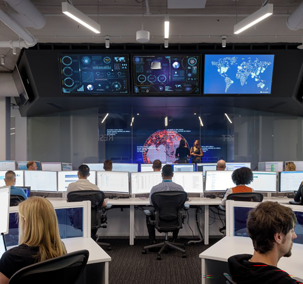 View from behind a group of people working at desktop computers in a room with a global map and status screens
